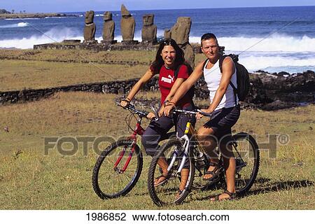 Stock Image - Easter Island, Couple On Bikes Near Tahai Beach, Moai Platform Sculptures In Background.. Fotosearch