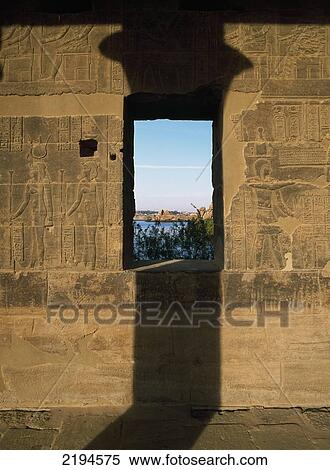 Stock Photography - Egypt, Aswan, Temple of Isis; Philae Island, Wall of West Colonnade covered in reliefs and hieroglyphs with shadow of column and window to Lake Nasser. Fotosearch