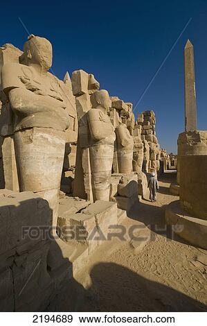 Egypt, Karnak Temple; Luxor, Egyptian temple attendant walking past line of statues in mummy position towards Hatshepsut's obelisk in Precinct of Amun View Large Photo Image Stock Photo - Egypt, Karnak Temple; Luxor, Egyptian temple attendant walking past line of statues in mummy position towards Hatshepsut's obelisk in Precinct of Amun. Fotosearch