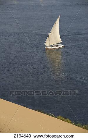 Stock Image - Egypt, Looking down on felucca from large sand dunes beside River Nile; Aswan. Fotosearch