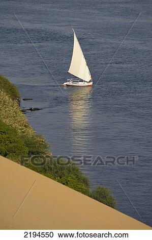Stock Image - Egypt, Looking down on felucca from large sand dunes beside River Nile; Aswan. Fotosearch