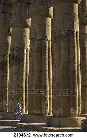 Egypt, Luxor Temple; Luxor, Temple guard sitting at base of papyrus-bundle columns with bud capitals in Court of Amenophis III View Large Photo Image Stock Image - Egypt, Luxor Temple; Luxor, Temple guard sitting at base of papyrus-bundle columns with bud capitals in Court of Amenophis III. Fotosearch
