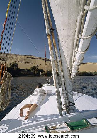 Stock Photo - Egypt, Woman lying on bow of felucca on River Nile in front of large sand dune; Aswan. Fotosearch