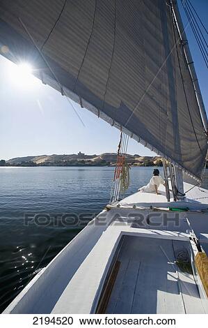 Stock Image - Egypt, Woman relaxing on deck of felucca going down River Nile; Aswan. Fotosearch