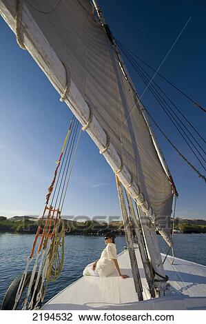 Stock Image - Egypt, Woman relaxing on deck of felucca going down River Nile; Aswan. Fotosearch