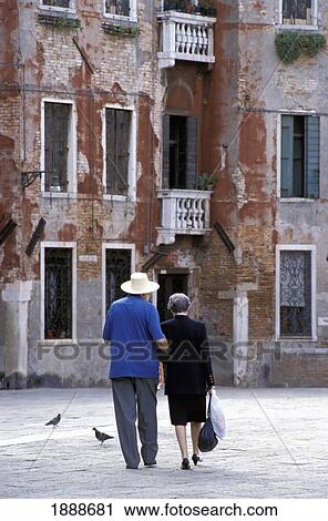 Stock Image - Elderly Couple Walking Near Run Down Buildings. Fotosearch