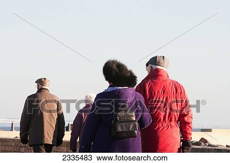 Stock Image - Elderly Couples Going For Walk Along Waterfront Near West Bay Harbor; Jurassic Coast, Dorset, England, Uk. Fotosearch