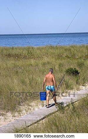 Stock Photography - Elderly Man Walking On Wooden Beach Walkway Carrying Fishing Rod. Fotosearch