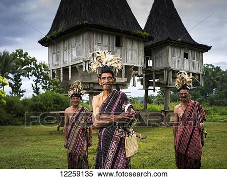 Stock Photography - Elderly men in traditional attire standing in front of distinctive houses; Timor-Leste. Fotosearch