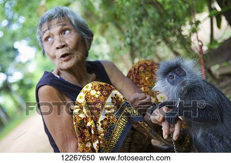 Stock Image - Elderly woman and monkey she raised; Battambang, Cambodia. Fotosearch
