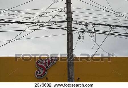 Stock Image - Electrical wires and phone cables with a sign on a yellow wall; Tulum, Mexico. Fotosearch