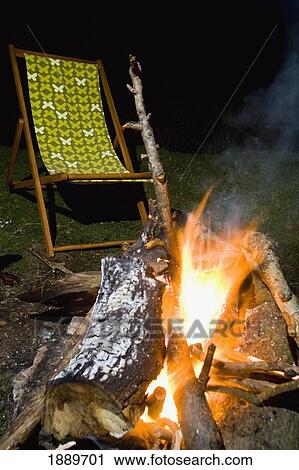 Stock Image - Empty Deck Chair And Wood Fire In The Evening. Fotosearch