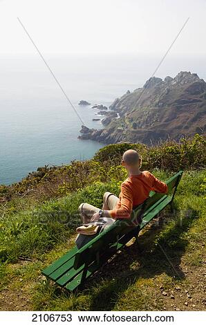 Stock Image - England, Guernsey, Tourist on bench; Le Gouffre. Fotosearch