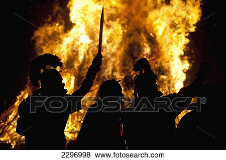 Stock Photo - England, Men dressed as Roman gladiators in front of bonfire at Battle Bonfire night; East Sussex. Fotosearch