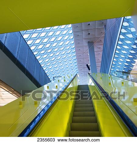 Stock Image - Escalator With Bright Yellow Sides And A Patterned Ceiling In Seattle Central Library; Seattle, Washington, United States Of America. Fotosearch