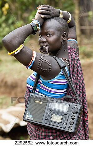 Ethiopia, Southern Nations Nationalities And Peoples' Region, South Omo, Portrait Of Mursi Tribal Woman With Pierced Lower Lip For Holding Pottery Lip-Plate (Dhebi) Walking With Radio; Jinka View Large Photo Image Stock Image - Ethiopia, Southern Nations Nationalities And Peoples' Region, South Omo, Portrait Of Mursi Tribal Woman With Pierced Lower Lip For Holding Pottery Lip-Plate (Dhebi) Walking With Radio; Jinka. Fotosearch