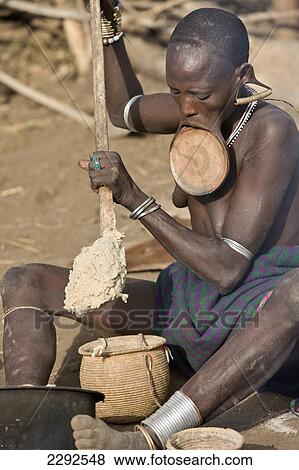 Stock Photo - Ethiopia, Southern Nations Nationalities And Peoples' Region, South Omo, Mursiland, Mursi Tribal Woman With Large Pottery Lip-Plate (Dhebi) Cooking Porridge; Mirobe Village. Fotosearch