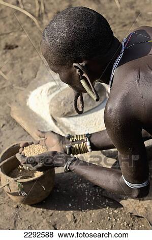 Ethiopia, Southern Nations Nationalities And Peoples' Region, South Omo, Mursiland, Mursi Tribal Woman Grinding Sorghum Grains For Cooking Porridge; Mirobe Village View Large Photo Image Stock Photo - Ethiopia, Southern Nations Nationalities And Peoples' Region, South Omo, Mursiland, Mursi Tribal Woman Grinding Sorghum Grains For Cooking Porridge; Mirobe Village. Fotosearch