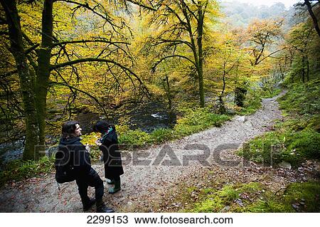 Stock Image - Exmoor National Park; Malaysia, Tourists crossing Tarr Steps Circular walk near Tarr Steps are prehistoric clapper bridge across River Barle. Fotosearch