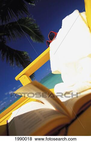 Stock Photo - Extreme Close-Up Of A Book, Glasses And Towel On Beach Chair, Dark Blue Sky. Fotosearch