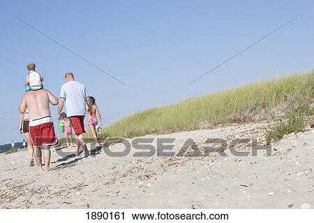 Stock Image - Family Walking By Grassy Sand Dunes On Beach. Fotosearch