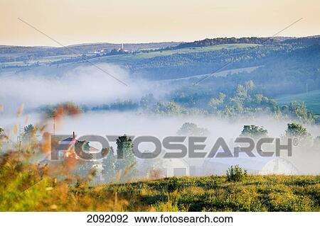 Stock Image - Farm Structures Through Fog; Chesterville Quebec Canada. Fotosearch