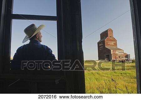 Stock Photograph - Farmer Looking Towards An Abandoned Grain Elevator, In The Ghost Town Of Bents, Saskatchewan. Fotosearch