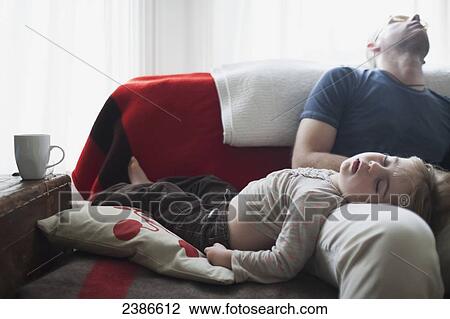 Stock Image - Father and daughter crashed out asleep on sofa; Toronto, Ontario, Canada. Fotosearch