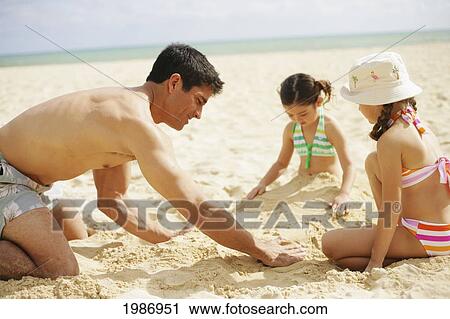 Stock Image - Father And Daughters Playing In The Sand On A Warm Tropical Beach.. Fotosearch