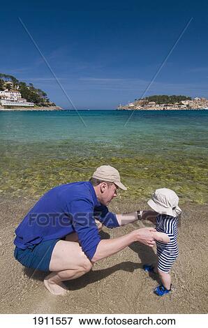 Stock Photo - Father Holding Baby Boy (6-11 Months) By Hands On Beach, Soller, Majorca, Balearic Islands, Spain. Fotosearch