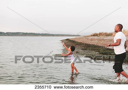 Stock Image - Father Wading In Water With Daughter; British Columbia, Canada. Fotosearch