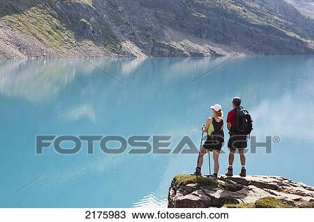 Stock Image - Female And Male Hikers On Rock Cliff Overlooking Mountain Lake; Field British Columbia Canada. Fotosearch