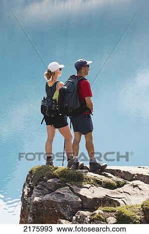 Stock Image - Female And Male Hikers On Rock Cliff Overlooking Mountain Lake; Field British Columbia Canada. Fotosearch