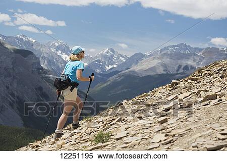Female hiker with poles hiking up a rocky mountain ridge with valleys and mountains in the background with blue sky and clouds; Alberta, Canada View Large Photo Image Stock Photography - Female hiker with poles hiking up a rocky mountain ridge with valleys and mountains in the background with blue sky and clouds; Alberta, Canada. Fotosearch