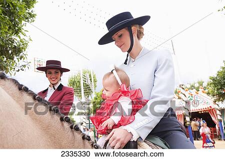 Stock Image - Female Horse Riders With A Child During April Feria Festival; Seville, Andalucia, Spain. Fotosearch