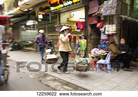 Female street vendor carries two baskets of various things in baskets suspended on each end of pole; Hanoi, Vietnam View Large Photo Image Stock Image - Female street vendor carries two baskets of various things in baskets suspended on each end of pole; Hanoi, Vietnam. Fotosearch