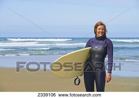 Stock Photograph - Female Surfer In Wetsuit Holding Surfboard On Wickaninnish Beach In Pacific Rim National Park; Tofino, Vancouver Island, British Columbia, Canada. Fotosearch