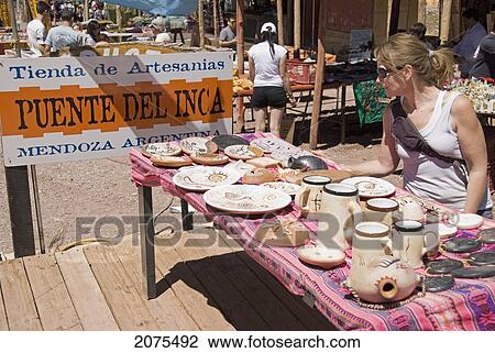 Stock Image - Female Tourist Examining Native Art On A Market Table In The Andes; Mendoza Argentina. Fotosearch