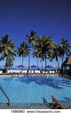 Stock Image - Fiji, Coral Coast, Shangri-La Resort, Woman Sunbathing In Pool, Palms And Blue Sky.. Fotosearch