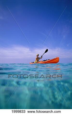 Stock Image - Fiji, Kadavu Island, Over/Under View Woman Orange Kayak, Calm Turquoise Ocean Blue Sky Wispy Clouds Lagoon. Fotosearch