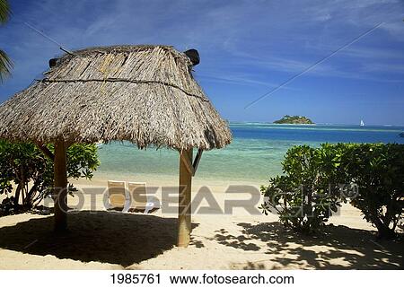 Stock Image - Fiji, Mamanuca Islands, Malolo Island, Beach With Two Beachchairs Under Grass Hut Beach Hut, /Nwadingi Island In Distance.. Fotosearch