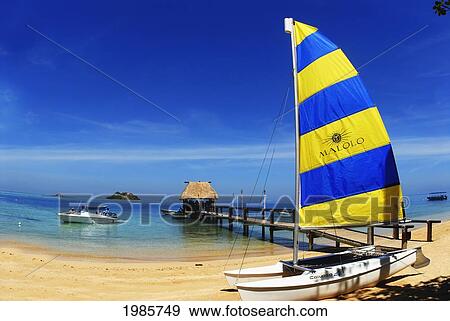 Fiji, Mamanuca Islands, Malolo Island, Hobbycat With Colorful Sail On White Sandy Beach Next To Pier With Bure Style Roof, Wanadigi Island In Background. View Large Photo Image Stock Photo - Fiji, Mamanuca Islands, Malolo Island, Hobbycat With Colorful Sail On White Sandy Beach Next To Pier With Bure Style Roof, Wanadigi Island In Background.. Fotosearch