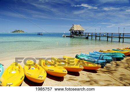 Stock Photo - Fiji, Mamanuca Islands, Malolo Island, Yellow And Blue Kayaks At The Beach Next To Pier With Bure Roof, Ocean, Wadigi Island And Sailboats/Nin Distance.. Fotosearch