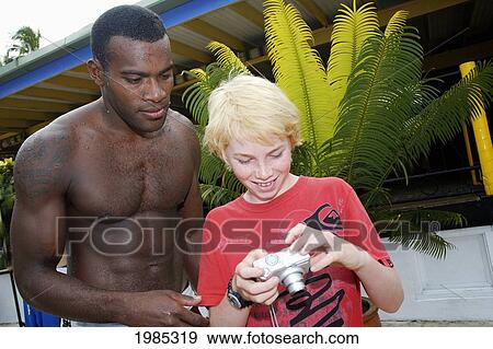 Fiji, Viti Levu, Coral Coast, Young Blond Tourist Boy Showing Photos On His Digital Camera To Fijian Man. For Editorial Use Only. View Large Photo Image Stock Photo - Fiji, Viti Levu, Coral Coast, Young Blond Tourist Boy Showing Photos On His Digital Camera To Fijian Man. For Editorial Use Only.. Fotosearch