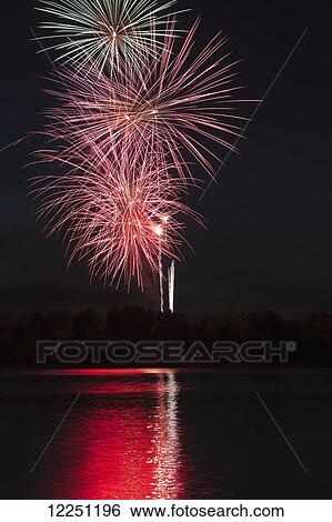 Stock Photograph - Fireworks reflecting off a lake with deep blue sky and a treed shoreline; Calgary, Alberta, Canada. Fotosearch