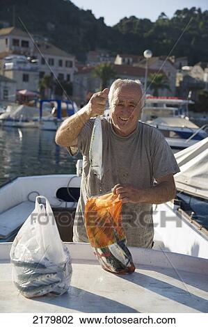 Fisherman holding up a fish in the harbour; Island of Lopud, Croatia View Large Photo Image Stock Image - Fisherman holding up a fish in the harbour; Island of Lopud, Croatia. Fotosearch