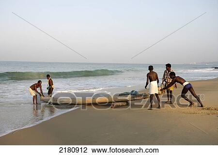 Stock Image - Fishermen pushing their boat from the beach into the water; Kovalam, Kerala, India. Fotosearch