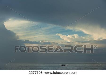 Stock Photo - Fishing boat with hole in stormy clouds behind, near Unawatuna; Sri Lanka. Fotosearch
