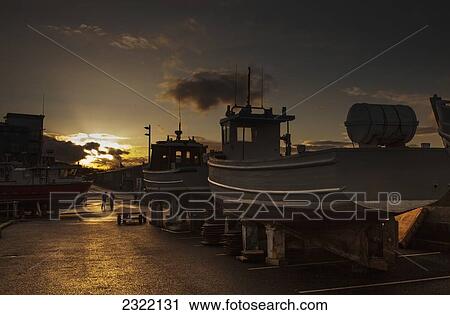 Stock Image - Fishing boats on lifts at sunset; Seahouses, Northumberland, England, UK. Fotosearch