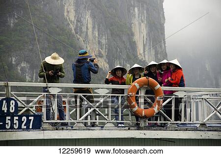 Five women wearing coolie hats line up for photo on top of passenger boat, and man looks at his camera; Halong Bay, Vietnam View Large Photo Image Stock Photo - Five women wearing coolie hats line up for photo on top of passenger boat, and man looks at his camera; Halong Bay, Vietnam. Fotosearch